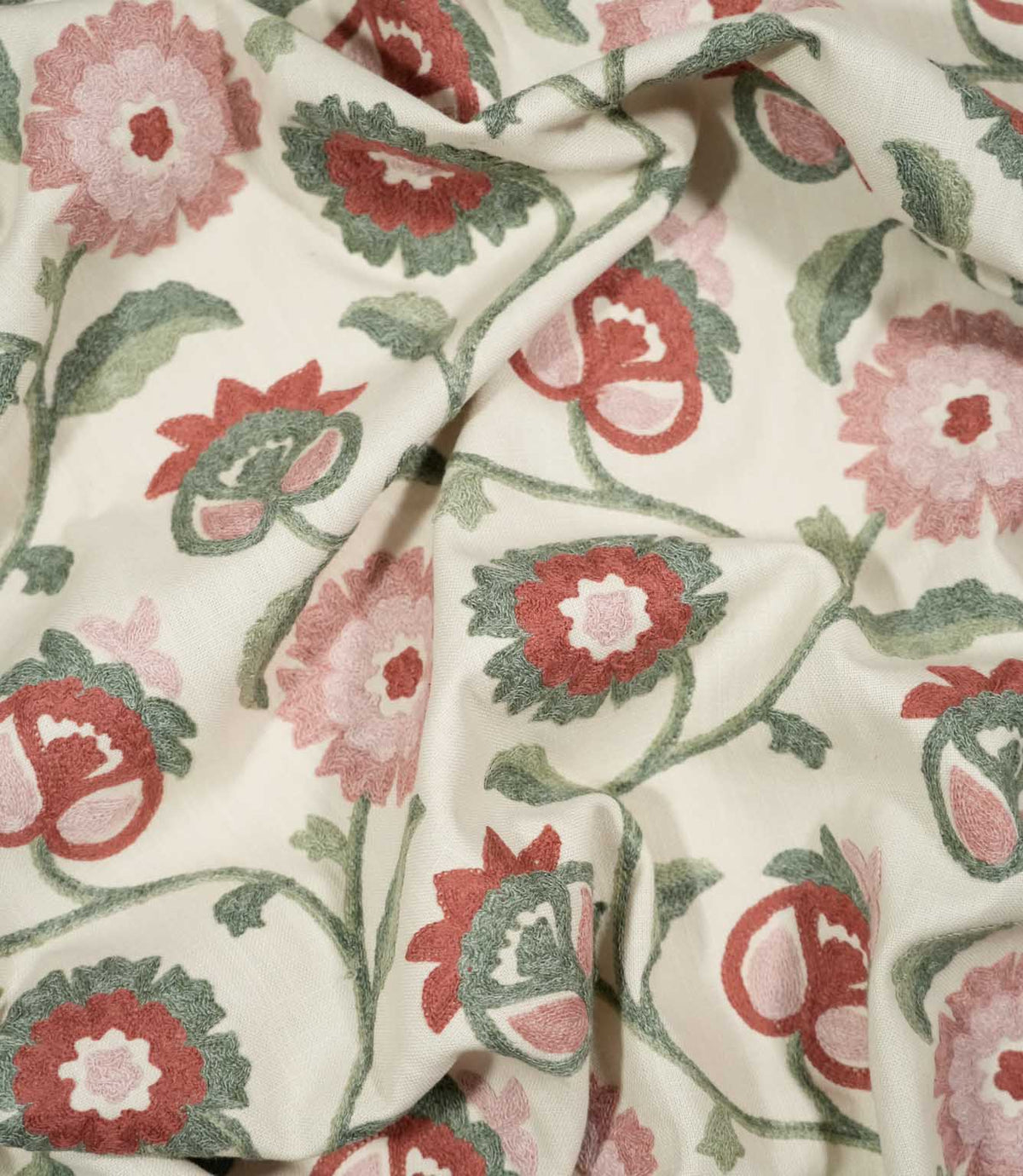 Foxmere Chintz embroidered fabric loosely draped into soft folds, showing how the decorative floral pattern falls across the cloth, with pink and muted red flowers connected by flowing sage green stems and leaves on a natural cream background.