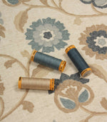 Foxmere Cornflower embroidered fabric shown with coordinating Gutermann thread spools, highlighting blue, grey and natural embroidery tones.