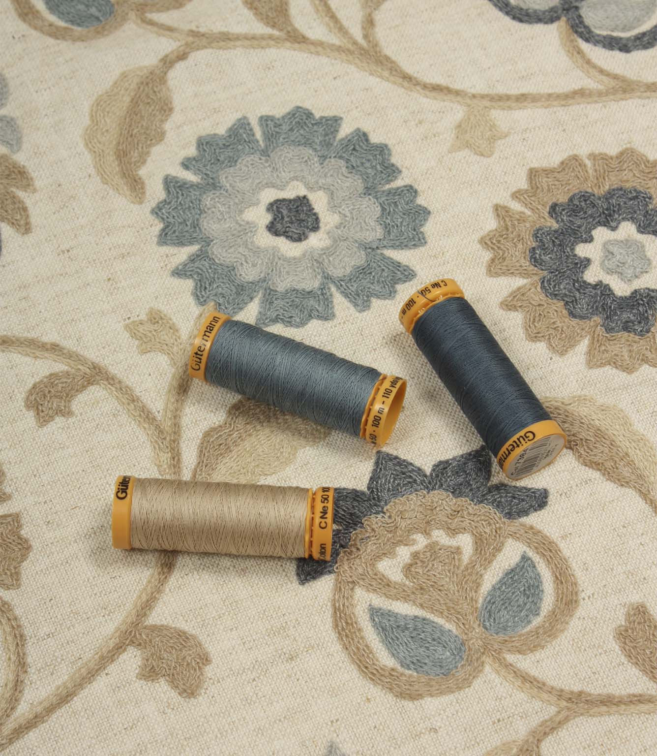 Foxmere Cornflower embroidered fabric shown with coordinating Gutermann thread spools, highlighting blue, grey and natural embroidery tones.