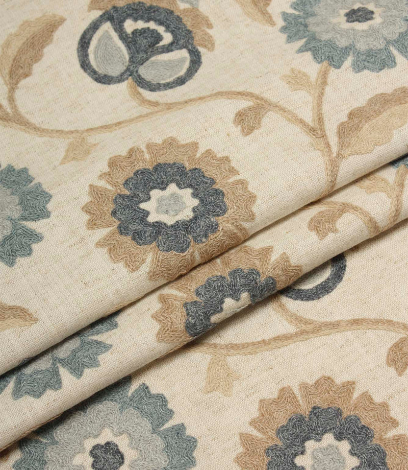 Folded Foxmere Cornflower fabric displaying detailed embroidered floral patterns and textured stitching on a natural linen-look base.