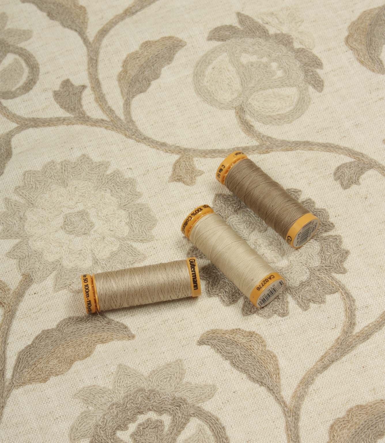 Foxmere Natural embroidered fabric displayed with coordinating neutral Gutermann thread spools to showcase matching tones.