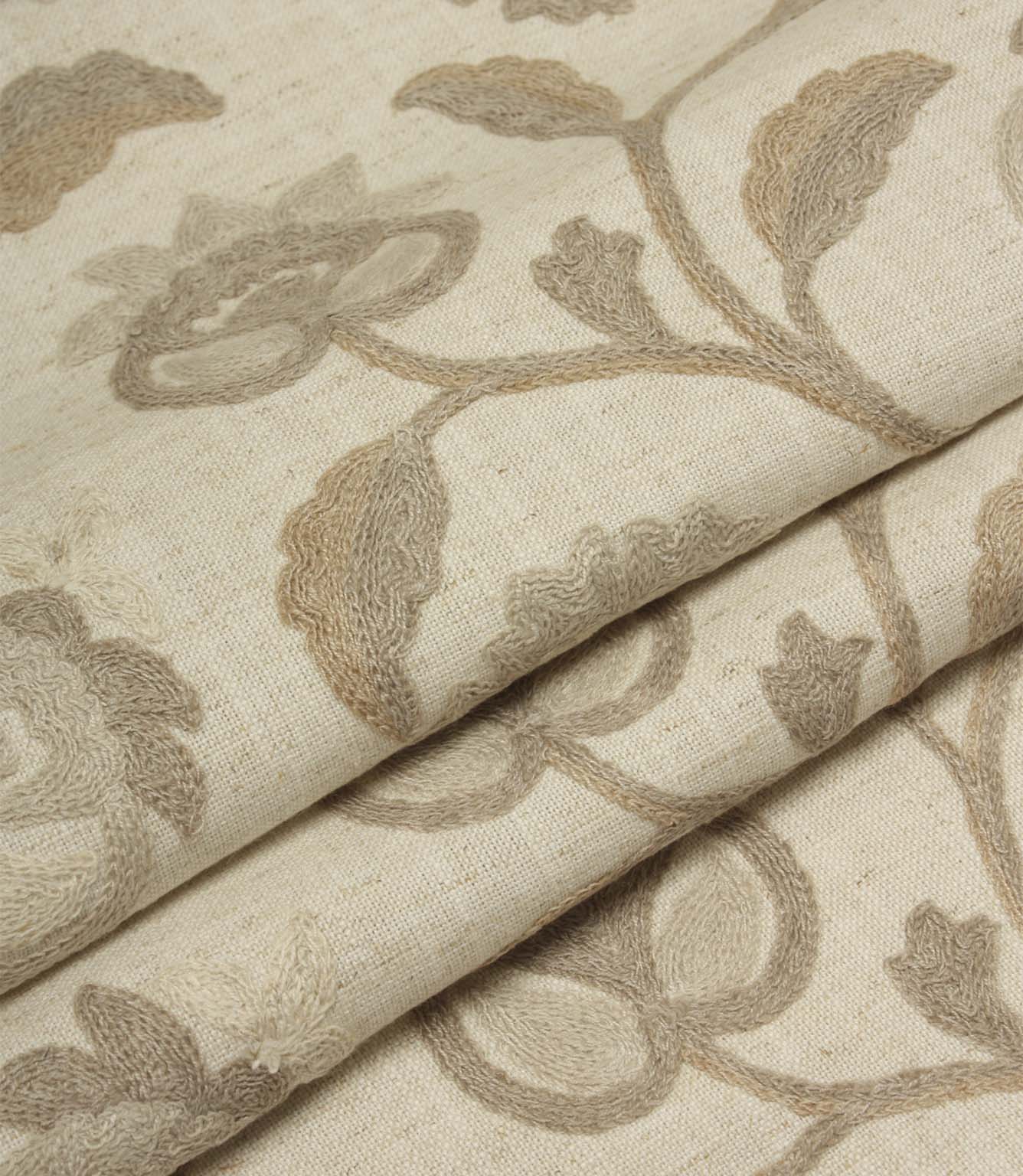 Folded natural embroidered fabric featuring intricate floral motifs and trailing vines on a soft woven base cloth.