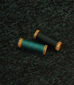 Galaxy emerald fabric displayed with coordinating thread spools, highlighting the deep green tones, abstract pattern and woven texture.