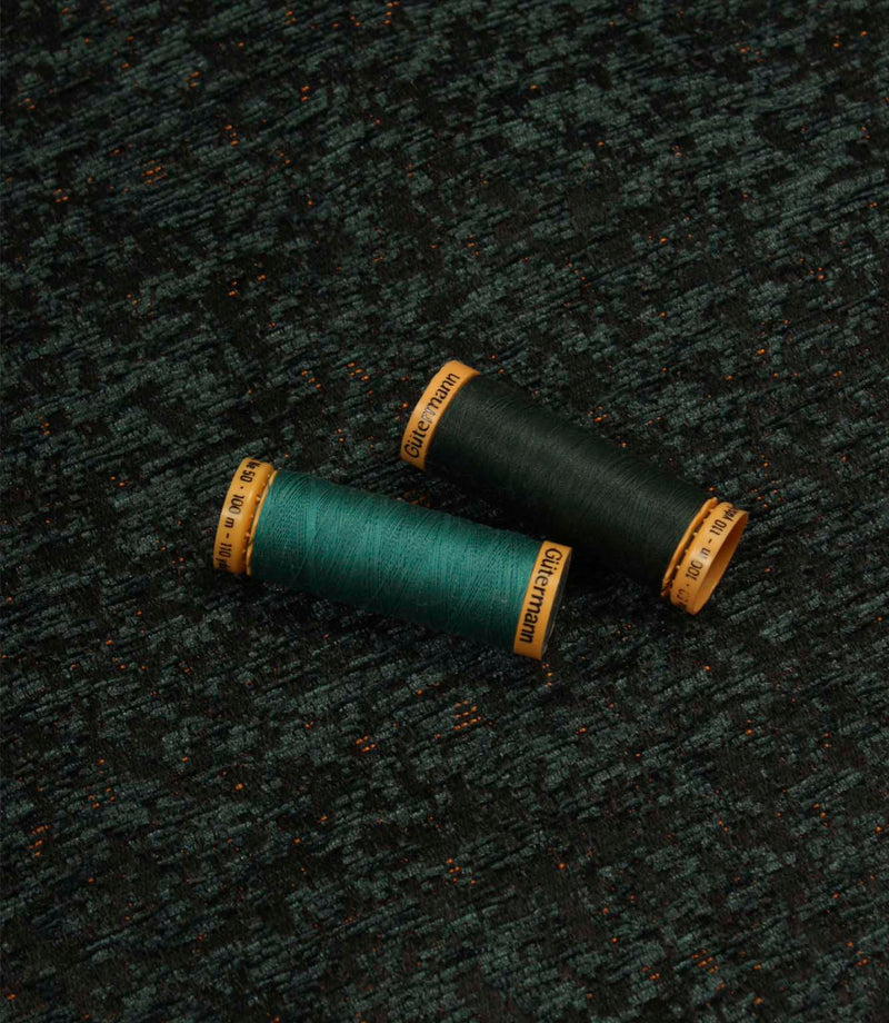 Galaxy emerald fabric displayed with coordinating thread spools, highlighting the deep green tones, abstract pattern and woven texture.