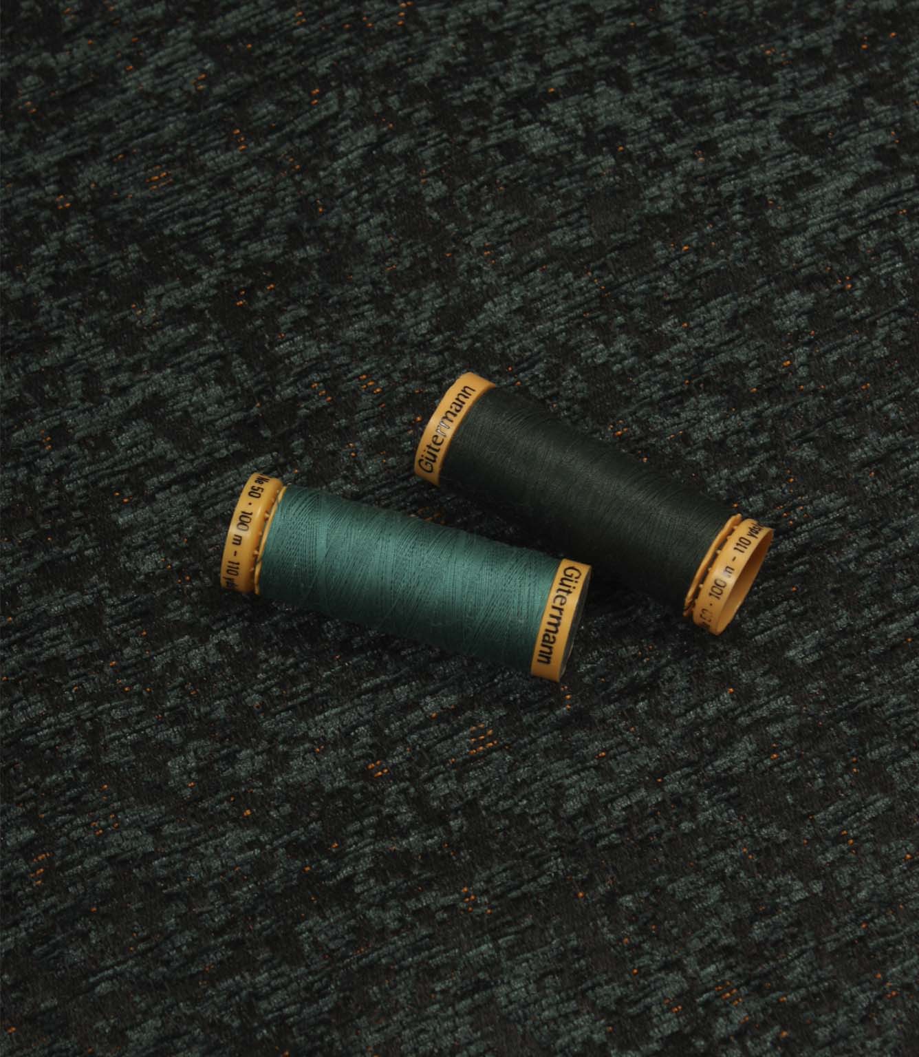 Galaxy emerald fabric displayed with coordinating thread spools, highlighting the deep green tones, abstract pattern and woven texture.