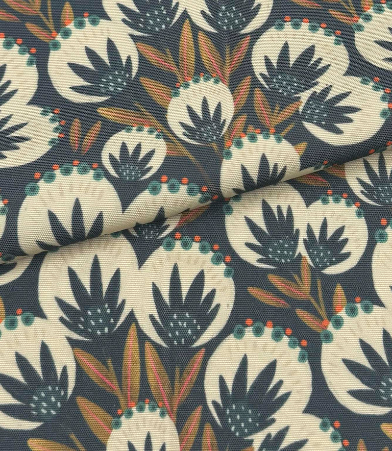 Folded Ember Crest outdoor fabric featuring cream botanical motifs with teal, coral, and ochre detailing on a deep navy background.
