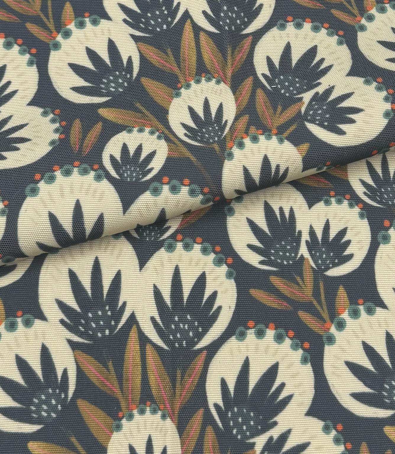 Folded Ember Crest outdoor fabric featuring cream botanical motifs with teal, coral, and ochre detailing on a deep navy background.