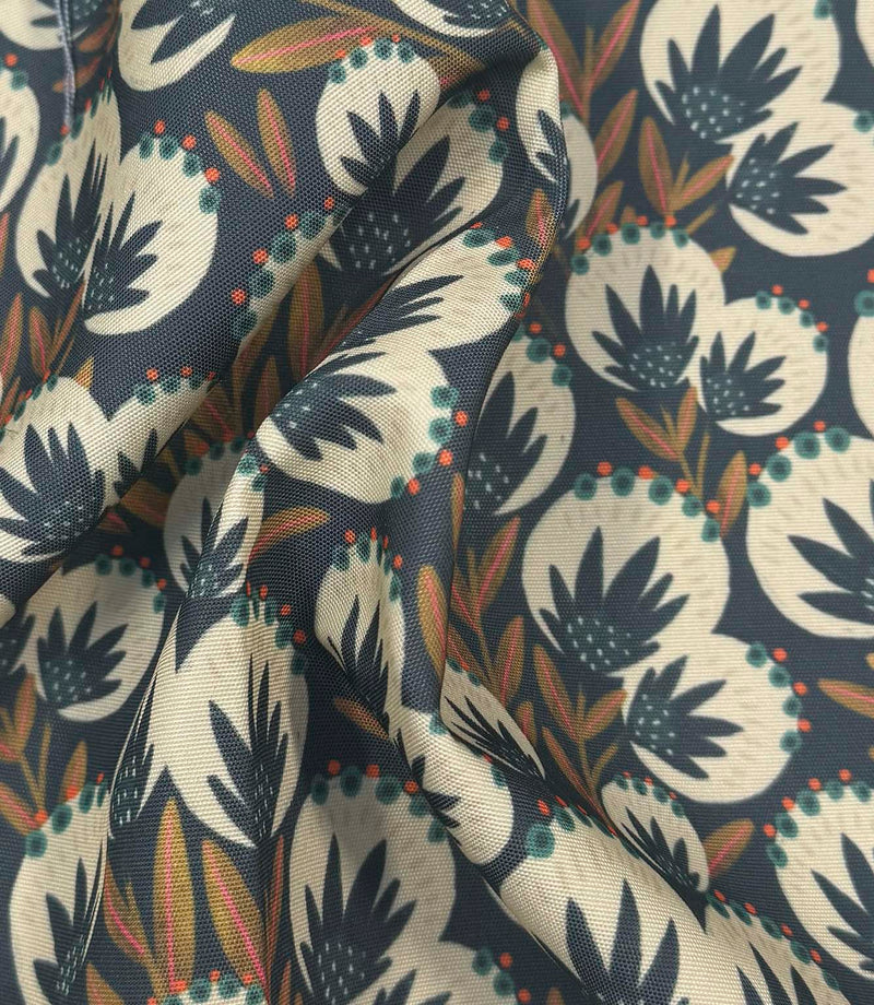 Draped Ember Crest outdoor upholstery fabric showing a decorative botanical pattern in navy, cream, coral, and olive shades.