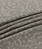 Close-up of Gardiner Gull fabric arranged in soft folds, showing the raised grey embroidered foliage pattern on a natural cream background and its textured finish.