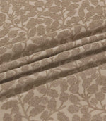 Close-up of Gardiner Rockpool fabric gathered into folds, displaying the taupe-brown embroidered foliage, textured leaf motifs and natural woven background.