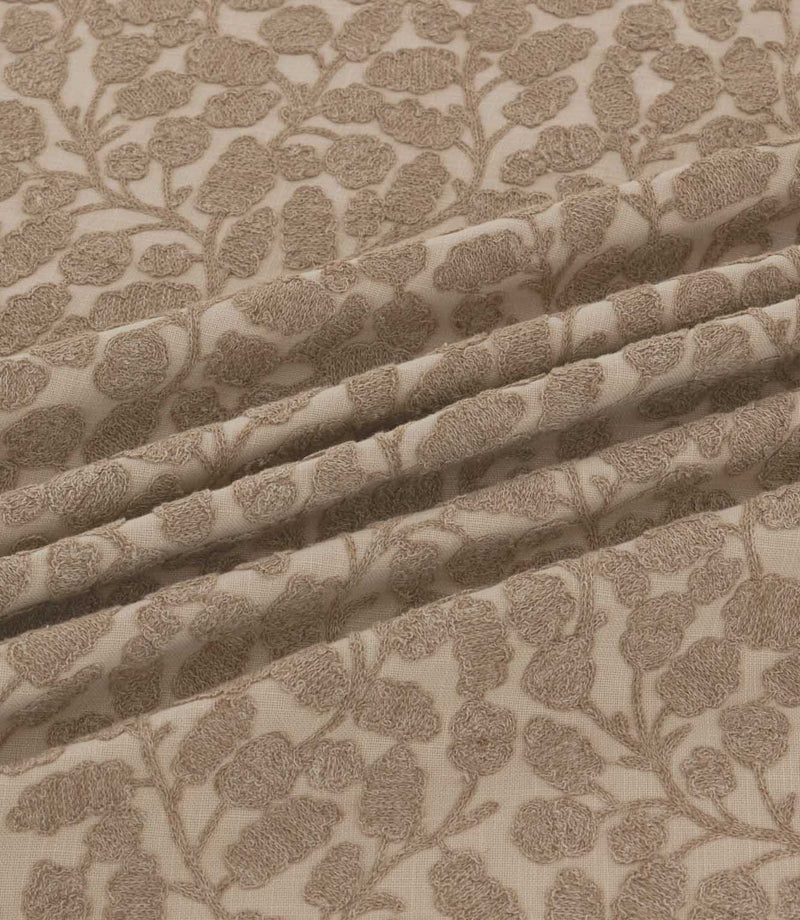 Close-up of Gardiner Rockpool fabric gathered into folds, displaying the taupe-brown embroidered foliage, textured leaf motifs and natural woven background.
