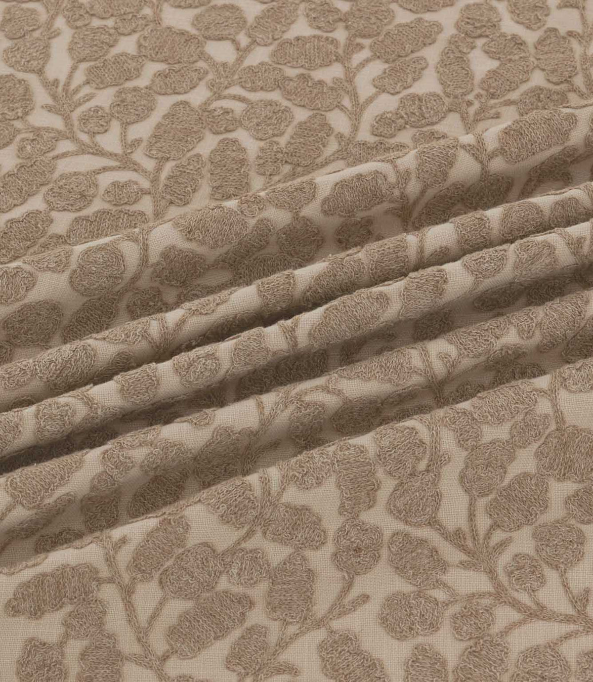 Close-up of Gardiner Rockpool fabric gathered into folds, displaying the taupe-brown embroidered foliage, textured leaf motifs and natural woven background.