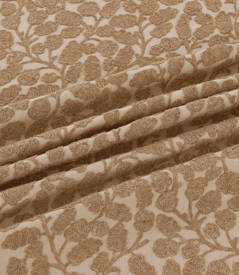 Close-up of Gardiner Sandytan fabric draped in soft folds, highlighting the warm sandy brown embroidered leaves, delicate stems and textured natural background.