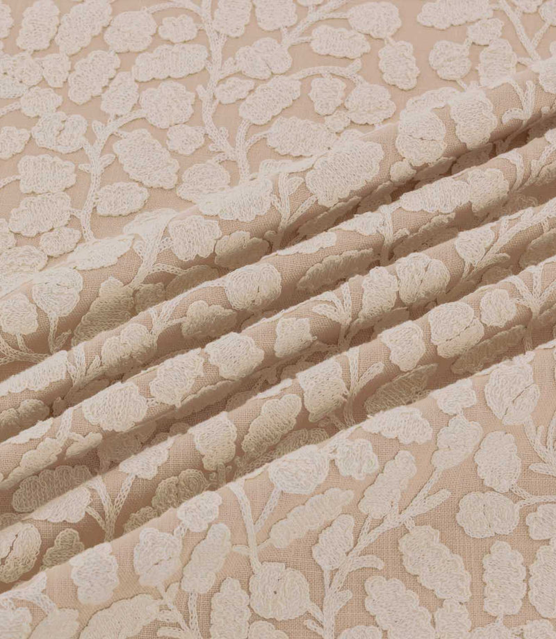 Gardiner Shell fabric gathered into gentle folds, showing the raised ivory embroidered botanical pattern against a blush-beige background and its detailed woven texture.