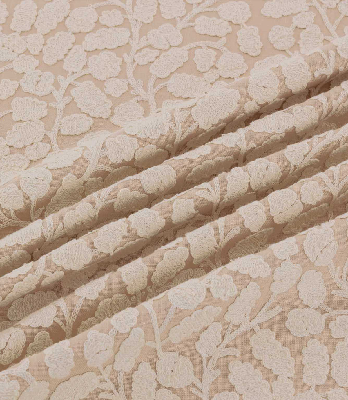 Gardiner Shell fabric gathered into gentle folds, showing the raised ivory embroidered botanical pattern against a blush-beige background and its detailed woven texture.