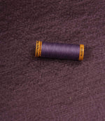 Glaze plum plain fabric with matching thread spool, highlighting its textured appearance and satin-inspired finish.