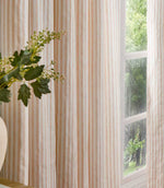 Blush pink and cream striped curtains hanging beside a large window, showing the full-length drape and classic vertical stripe design.