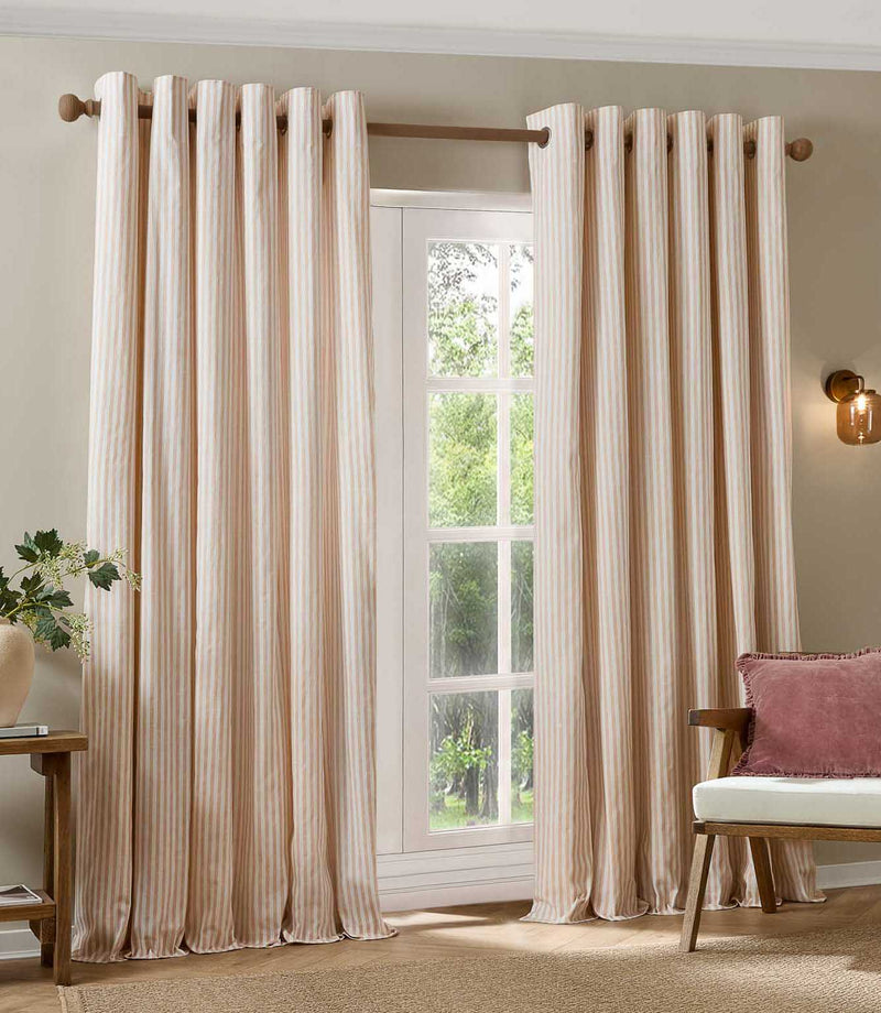 Pair of blush pink and cream striped eyelet curtains framing a large window, styled in a bright living room with natural wood furniture and a pink cushion