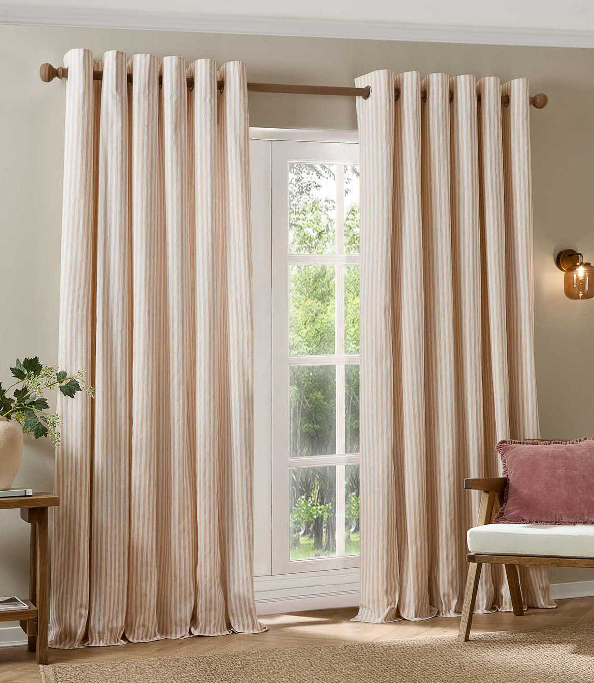 Pair of blush pink and cream striped eyelet curtains framing a large window, styled in a bright living room with natural wood furniture and a pink cushion