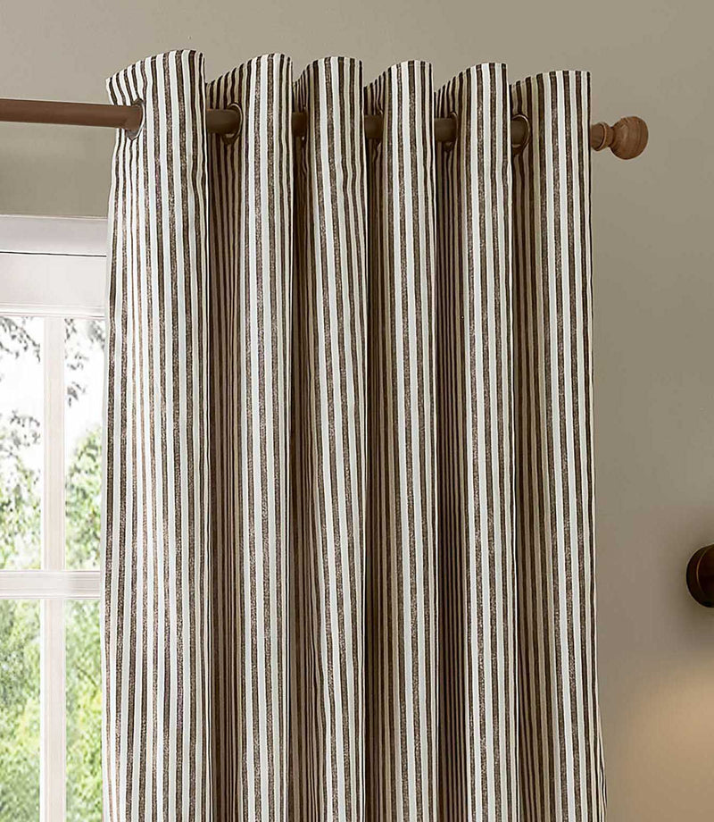 Close-up of brown and cream striped eyelet curtains on a wooden curtain pole, showing the metal eyelets, deep folds and narrow vertical stripe pattern.