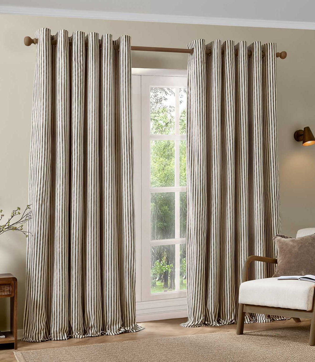 Pair of full-length brown and cream striped eyelet curtains framing a large window, styled in a neutral living room with a wooden armchair and natural textures.