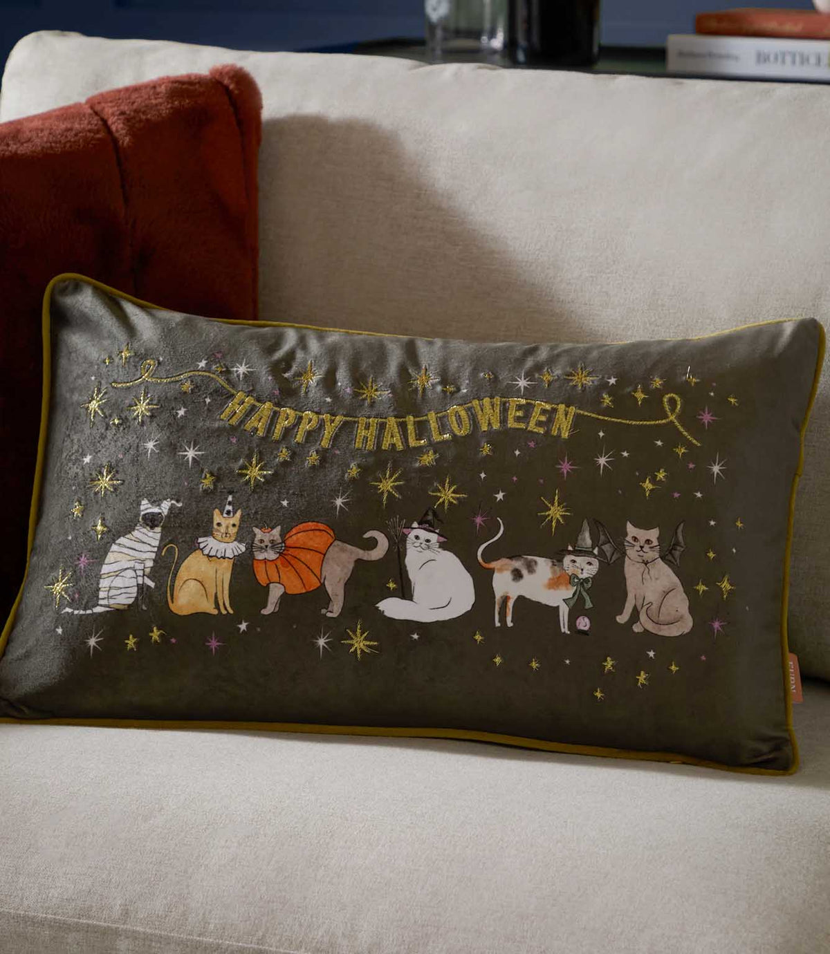 Halloween Pawty charcoal grey velvet cushion styled on a cream sofa, featuring gold Happy Halloween embroidery and multicoloured cats dressed in Halloween costumes.