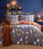 Halloween Pawty multicolour reversible duvet cover set with illustrated cats in witch, mummy, pumpkin and vampire costumes on a dusky blue background, styled with rust throws and cushions.