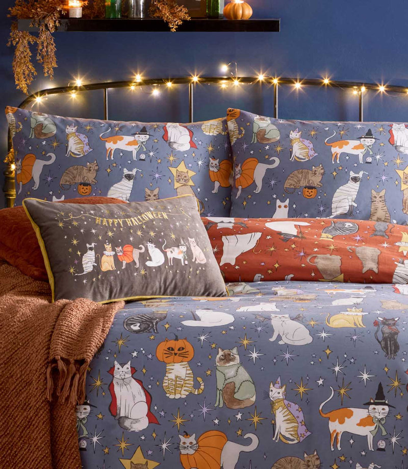 Close-up of the Halloween Pawty duvet cover and pillowcases showing multicoloured costumed cats, orange pumpkins and gold, white and purple stars on a dusky blue background.