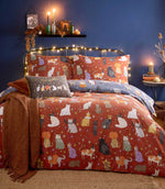 Halloween Pawty reversible duvet cover displayed on its rust-coloured side, featuring multicoloured cats in Halloween costumes with gold and purple stars, with the dusky blue reverse folded back.