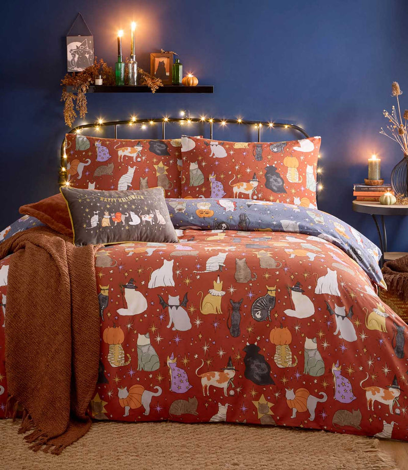 Halloween Pawty reversible duvet cover displayed on its rust-coloured side, featuring multicoloured cats in Halloween costumes with gold and purple stars, with the dusky blue reverse folded back.