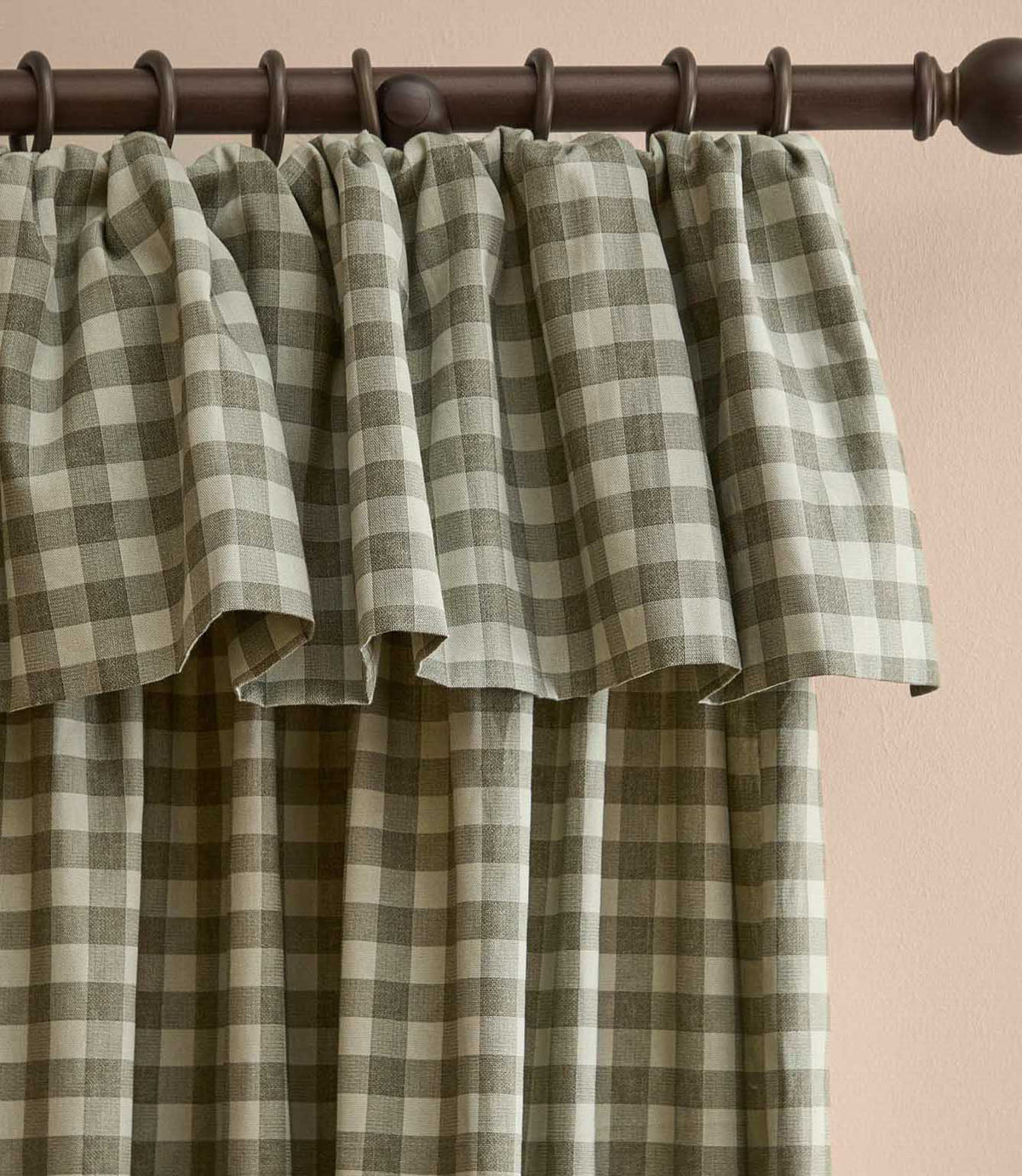 A close-up of a pleated curtain panel with a green and beige gingham plaid pattern, hanging from a dark brown metal rod against a light beige wall.