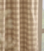 Close-up of natural beige and cream gingham check curtain fabric hanging beside a window, showing the lightweight woven cotton texture and soft drape.