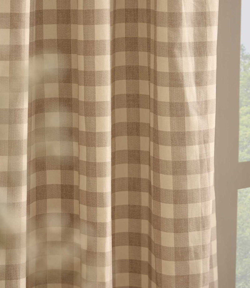 Close-up of natural beige and cream gingham check curtain fabric hanging beside a window, showing the lightweight woven cotton texture and soft drape.
