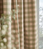 Close-up of Harriet pink and sage green gingham curtain fabric hanging beside a window, showing the woven texture, checked pattern and soft drape.