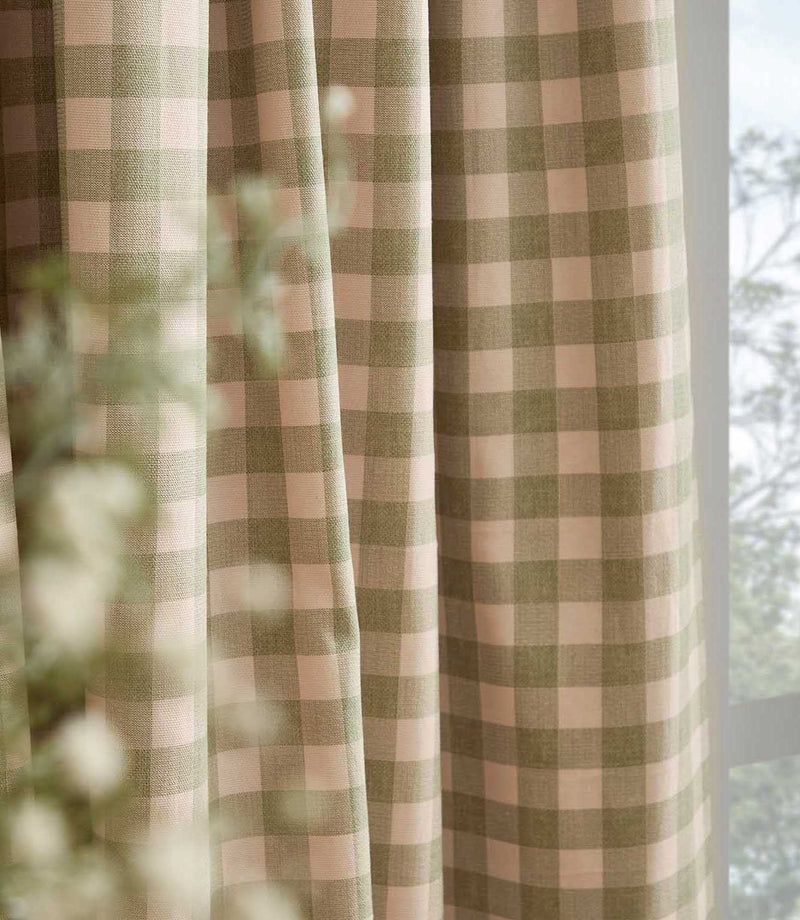 Close-up of Harriet pink and sage green gingham curtain fabric hanging beside a window, showing the woven texture, checked pattern and soft drape.