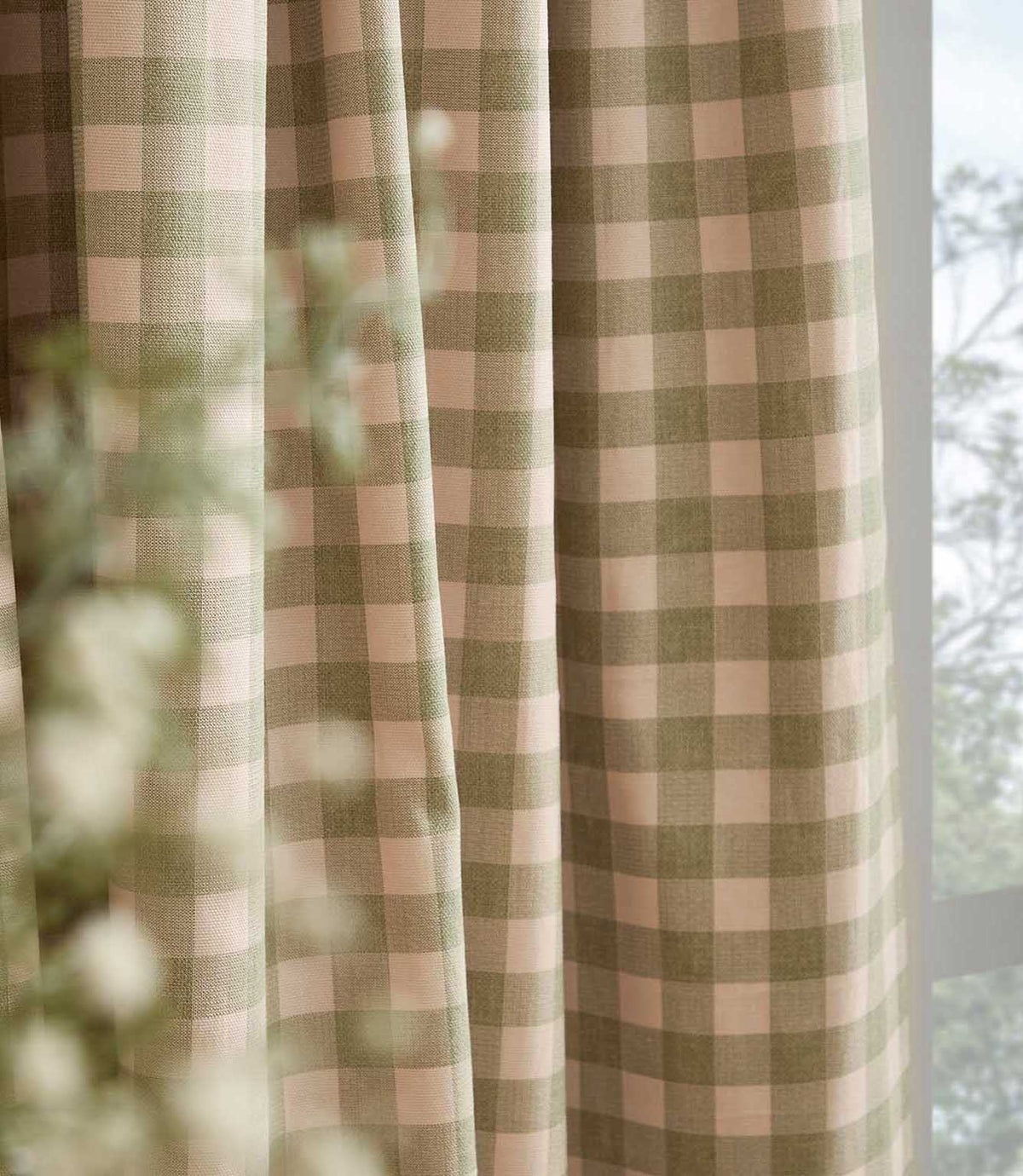 Close-up of Harriet pink and sage green gingham curtain fabric hanging beside a window, showing the woven texture, checked pattern and soft drape.