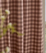 Close-up of Harriet pink and brown gingham curtain fabric hanging beside a window, showing the woven texture, classic check pattern and soft drape.