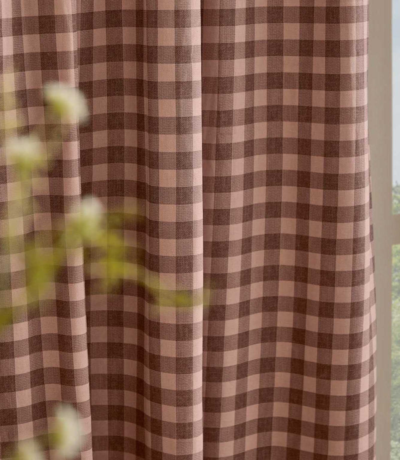 Close-up of Harriet pink and brown gingham curtain fabric hanging beside a window, showing the woven texture, classic check pattern and soft drape.