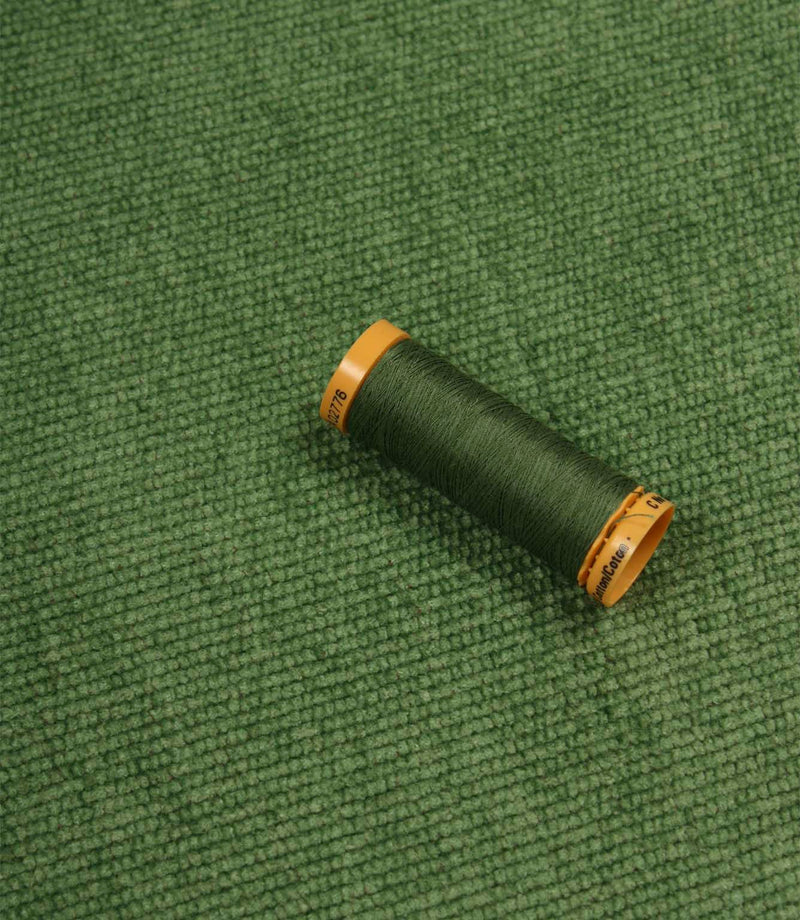 Hartwell emerald green upholstery fire retardant fabric displayed with a coordinating Gutermann thread spool.