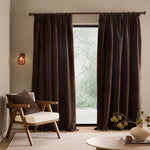Full-length espresso brown washed velvet curtains framing a large window in a neutral living room, styled with a wooden armchair and coordinating cushion.