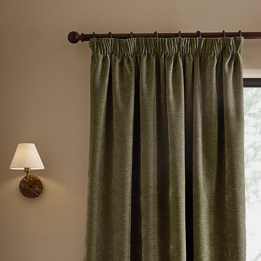 Eucalyptus green washed velvet pencil pleat curtain hanging from a dark wooden curtain pole, showing the gathered heading, deep folds and textured finish.