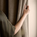 Close-up of a person holding a greige washed velvet curtain, showing the soft drape, subtle ribbed texture and gently mottled finish of the fabric.