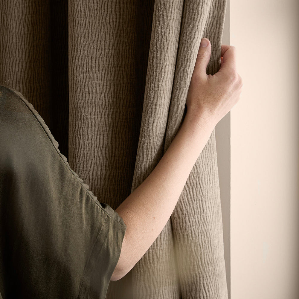 Close-up of a person holding a greige washed velvet curtain, showing the soft drape, subtle ribbed texture and gently mottled finish of the fabric.