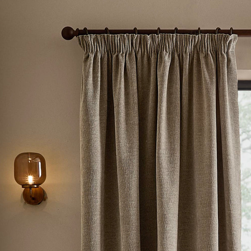 Greige washed velvet pencil pleat curtain hanging from a dark wooden curtain pole, showing the gathered heading, deep folds and textured velvet finish.