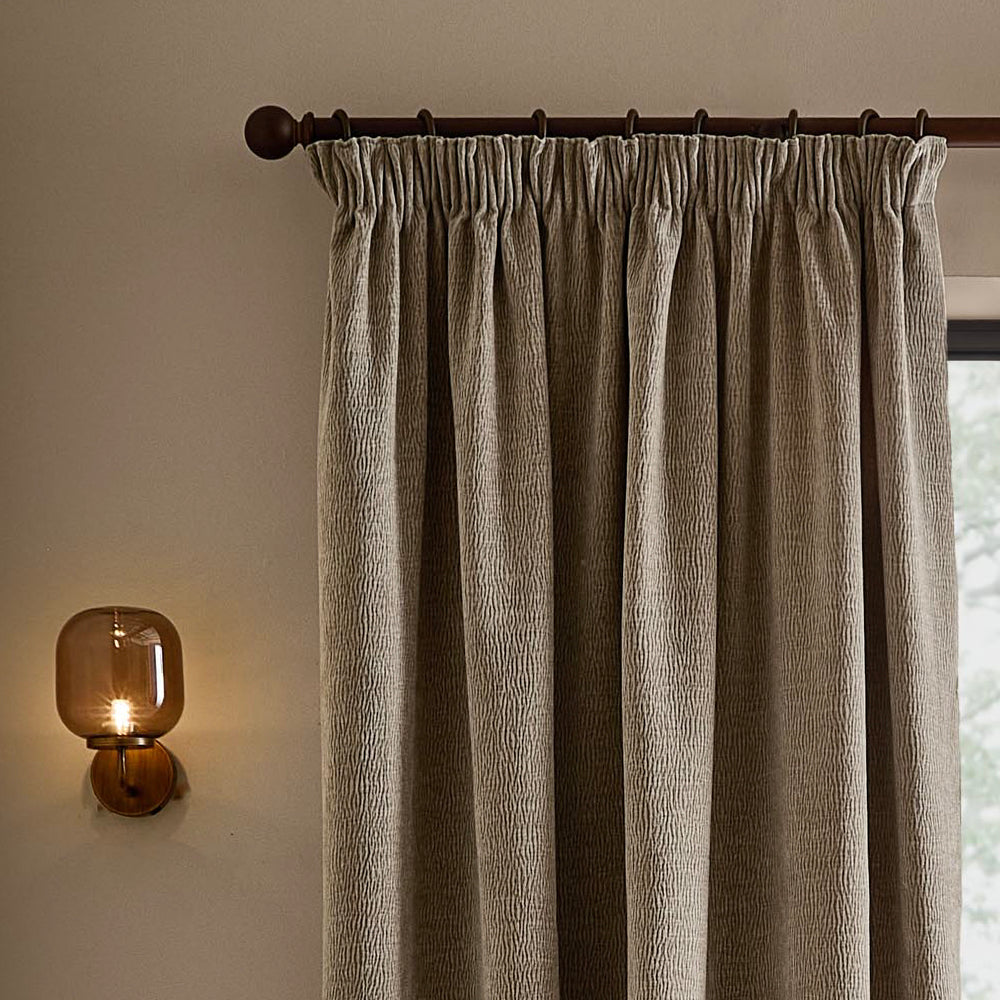 Greige washed velvet pencil pleat curtain hanging from a dark wooden curtain pole, showing the gathered heading, deep folds and textured velvet finish.