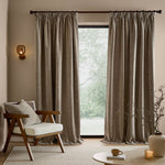 Full-length greige washed velvet curtains framing a large window in a neutral living room, styled with a wooden armchair, coordinating cushion and natural accessories.