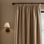 Natural linen beige washed velvet pencil pleat curtain hanging from a dark wooden curtain pole, showing the gathered heading, deep folds and textured velvet finish.