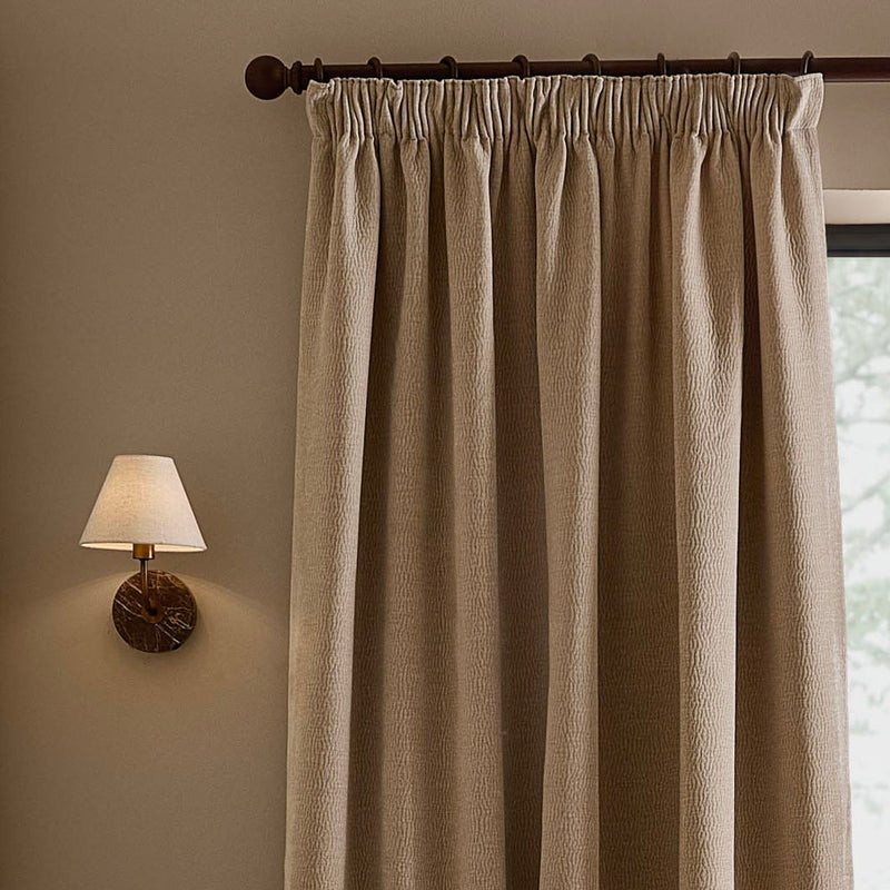 Natural linen beige washed velvet pencil pleat curtain hanging from a dark wooden curtain pole, showing the gathered heading, deep folds and textured velvet finish.
