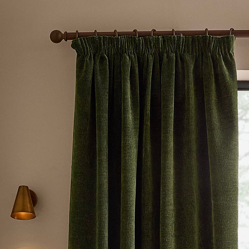 Olive green washed velvet pencil pleat curtain hanging from a dark wooden curtain pole, showing the gathered heading, deep folds and textured velvet surface.