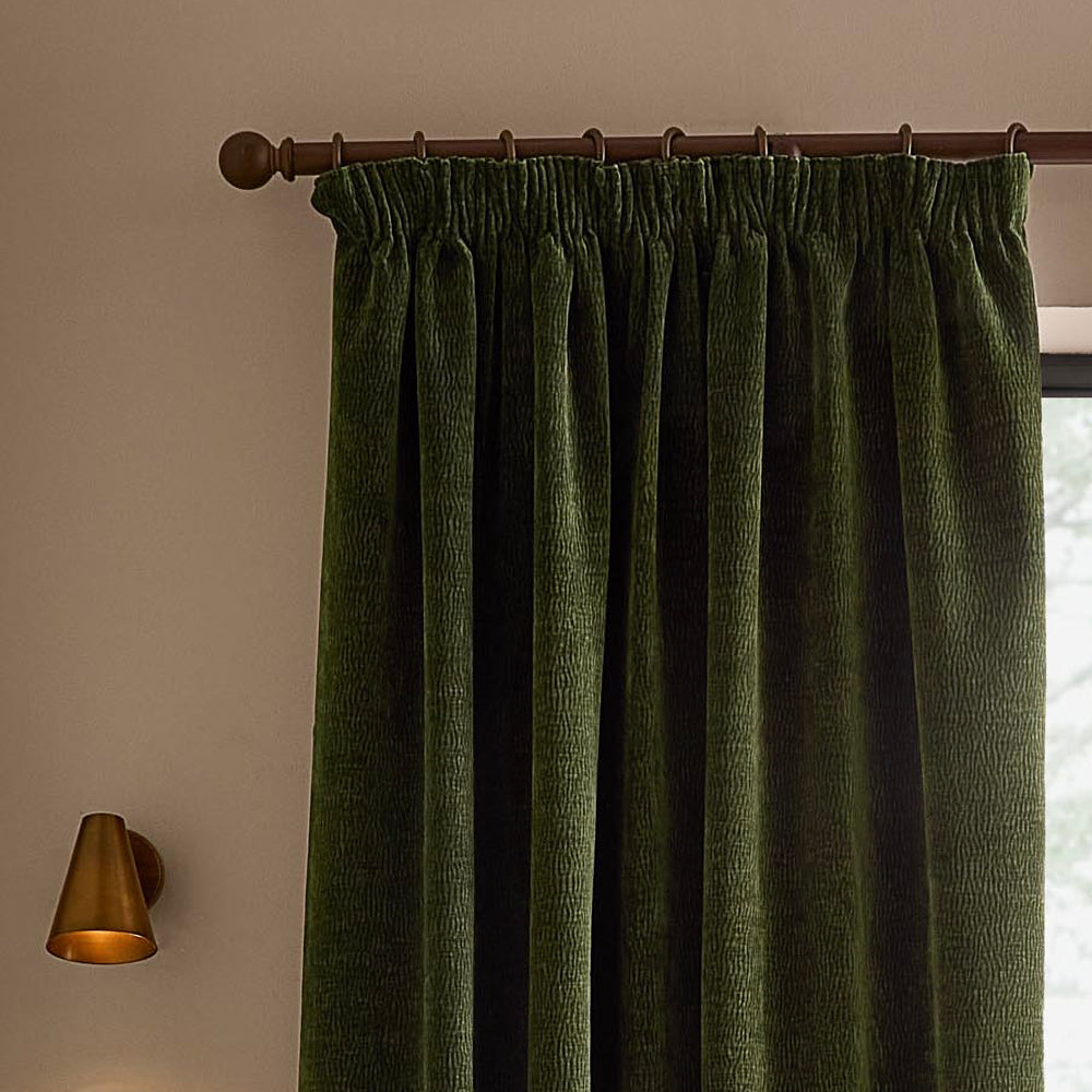 Olive green washed velvet pencil pleat curtain hanging from a dark wooden curtain pole, showing the gathered heading, deep folds and textured velvet surface.